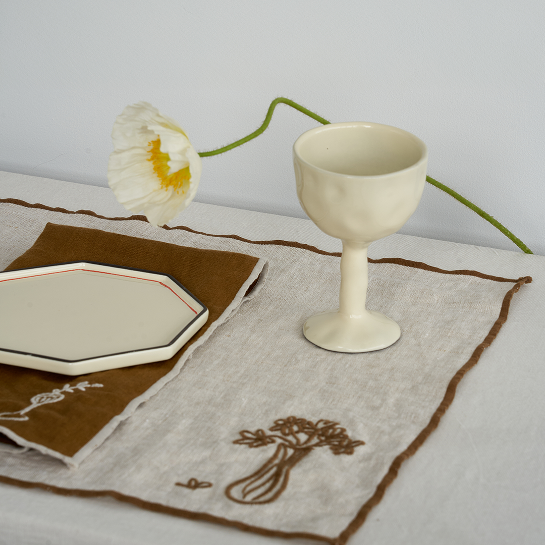 Ivory drinking glass goblet set by Black Blaze with a textured surface on a linen runner.