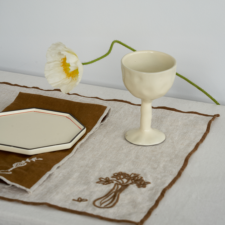 Ivory drinking glass goblet set by Black Blaze with a textured surface on a linen runner.