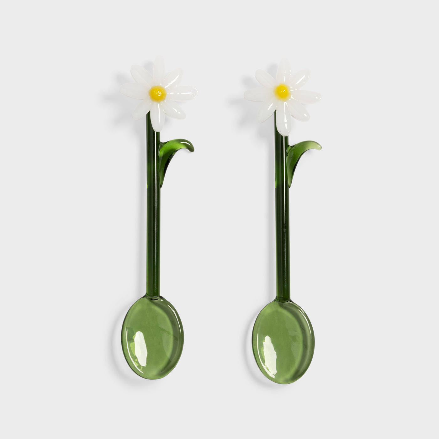 Two green spoons with daisy flower designs on a white background