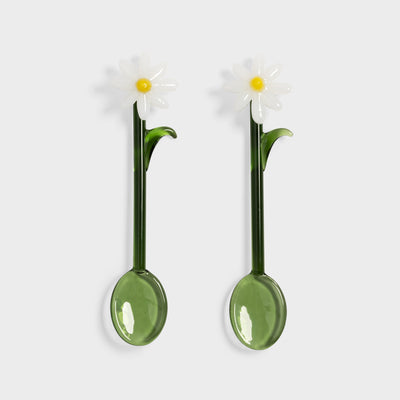 Two green spoons with daisy flower designs on a white background