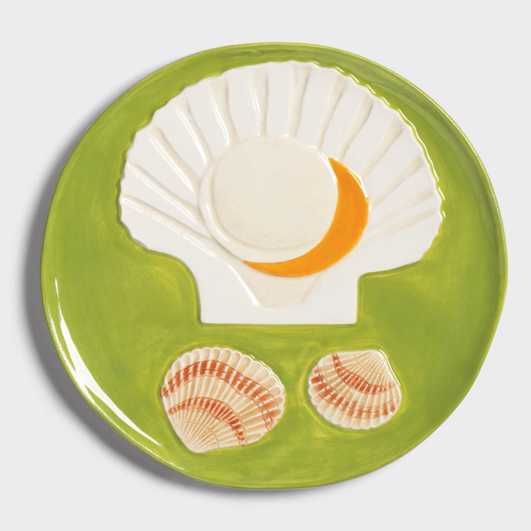 Ceramic decorative plate by &Klevering, featuring an embossed scallop shell design, on a green background.