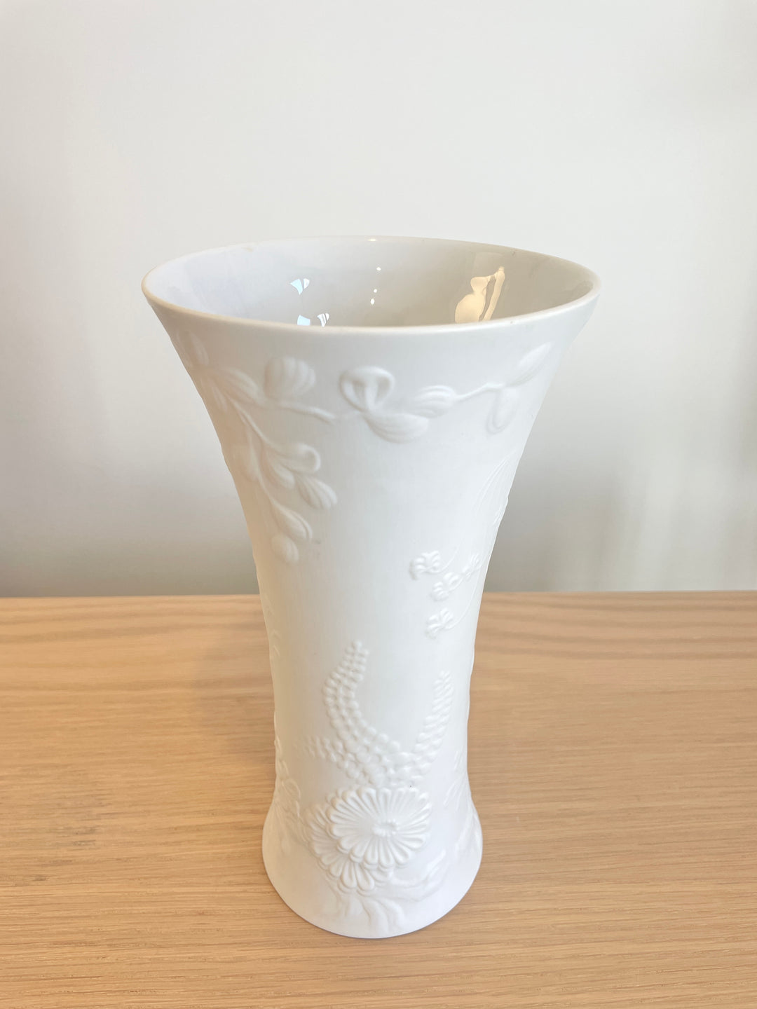 White porcelain vase by Kaiser featuring a floral relief design on a wooden surface