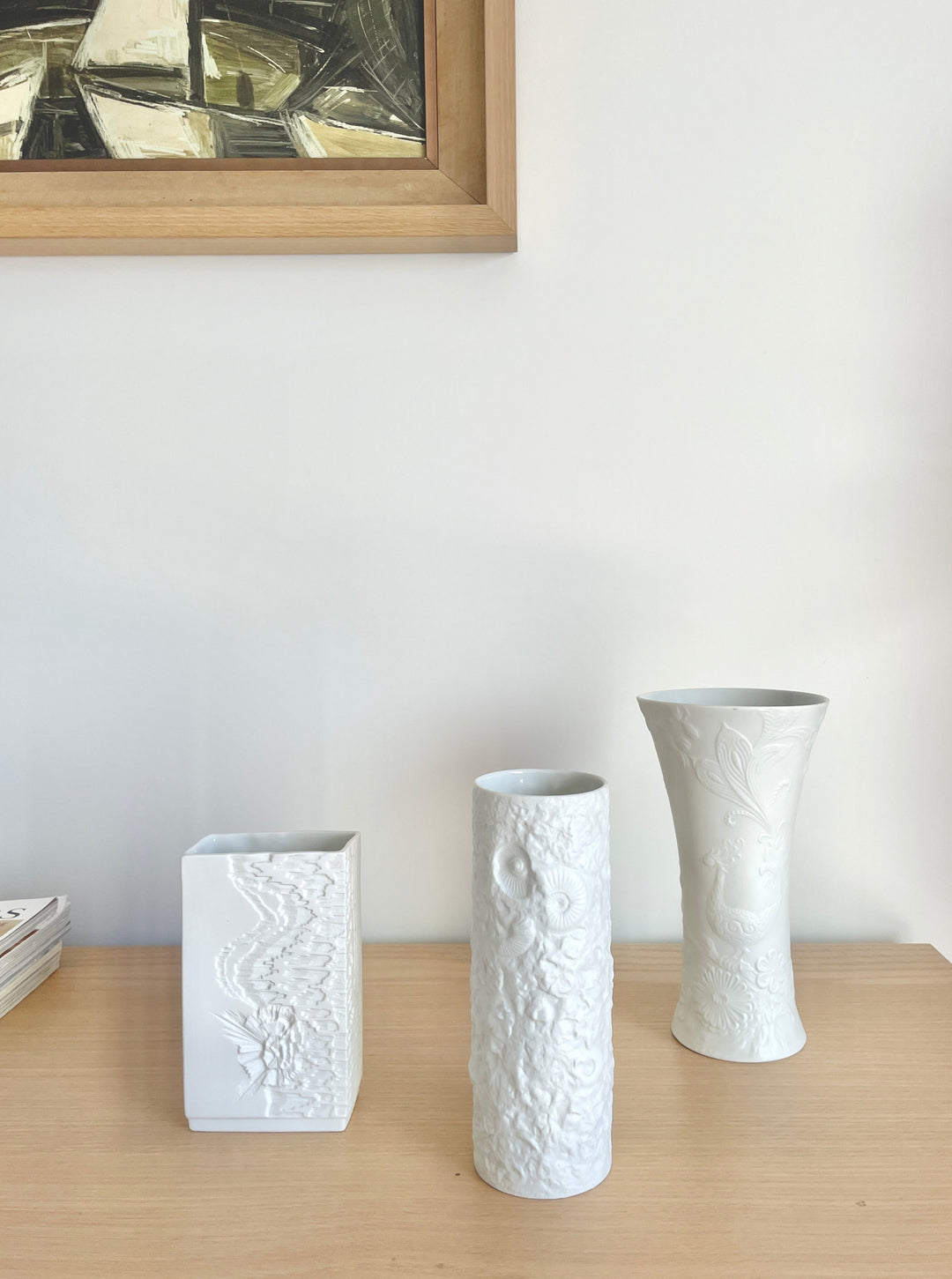 White porcelain vase by Kaiser, decorated with embossed floral and foliage designs, displayed on a wooden surface.
