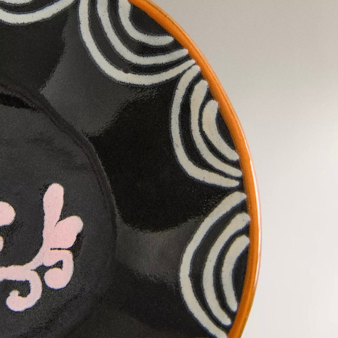 Painted earthware side plate from Nanushka with black glaze, pink floral design, and white striped pattern.
