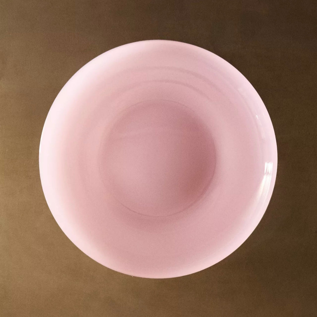 Pink colored dinner plate by Nanushka on a textured surface.

