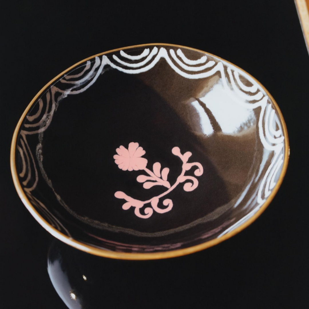 Decorative black dish with gold rim and pink floral design on a black background