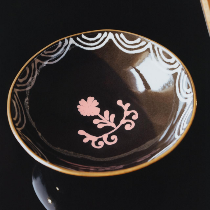 Decorative black dish with gold rim and pink floral design on a black background
