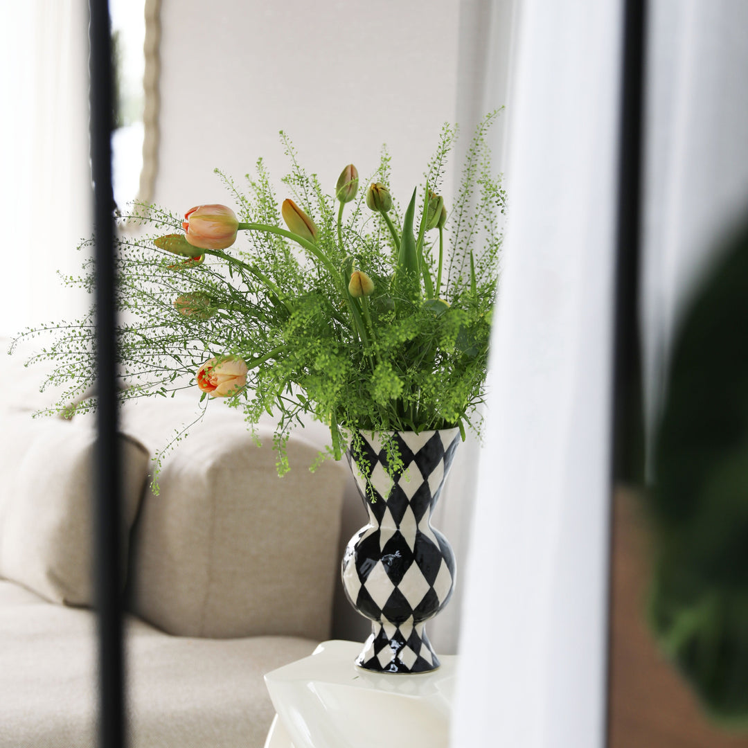 Black and white patterned rhombic vase by &Klevering with flowers, placed on a white table.