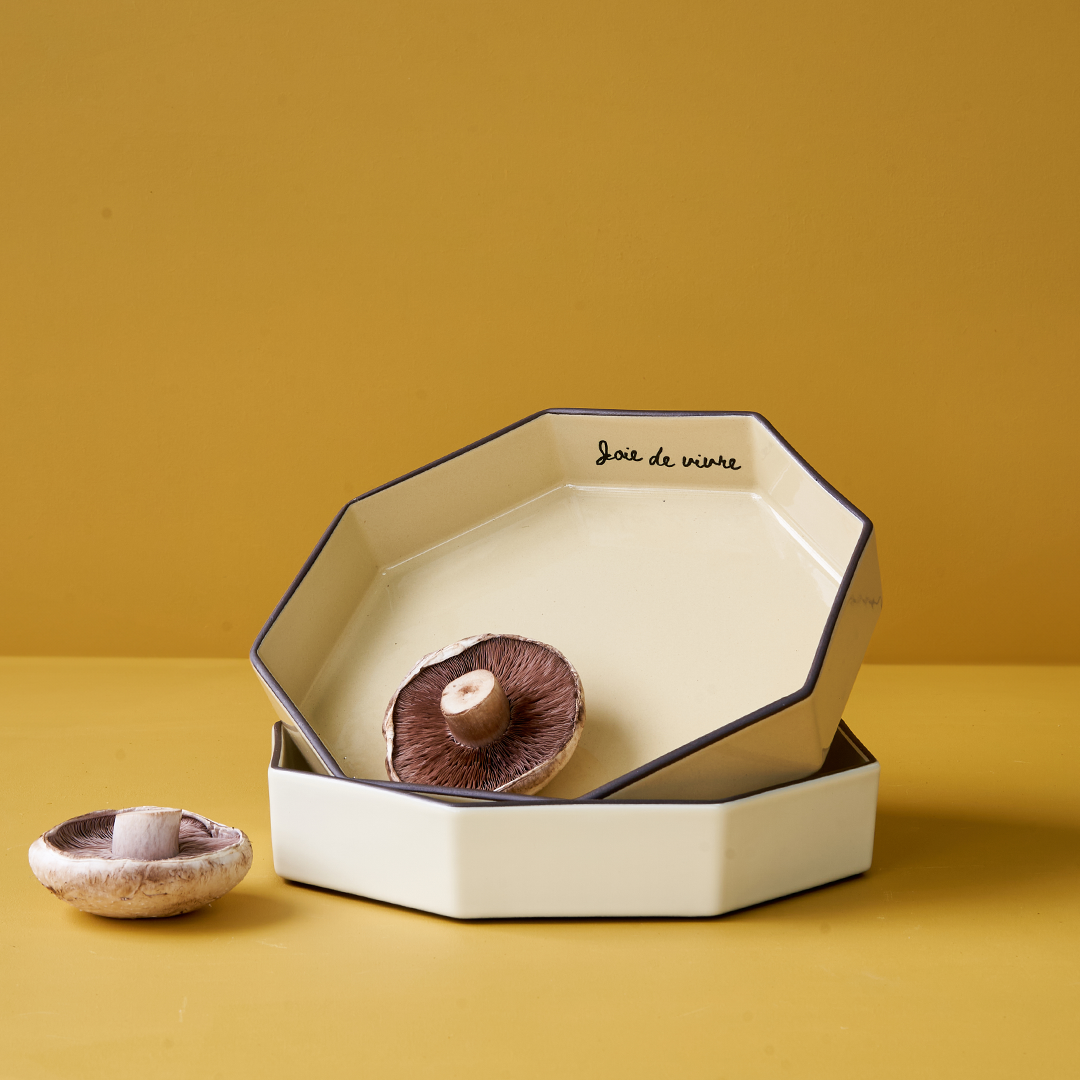 Wheat-colored Gem Bowl by Black Blaze with dark rim, stacked next to halved mushroom on yellow background.