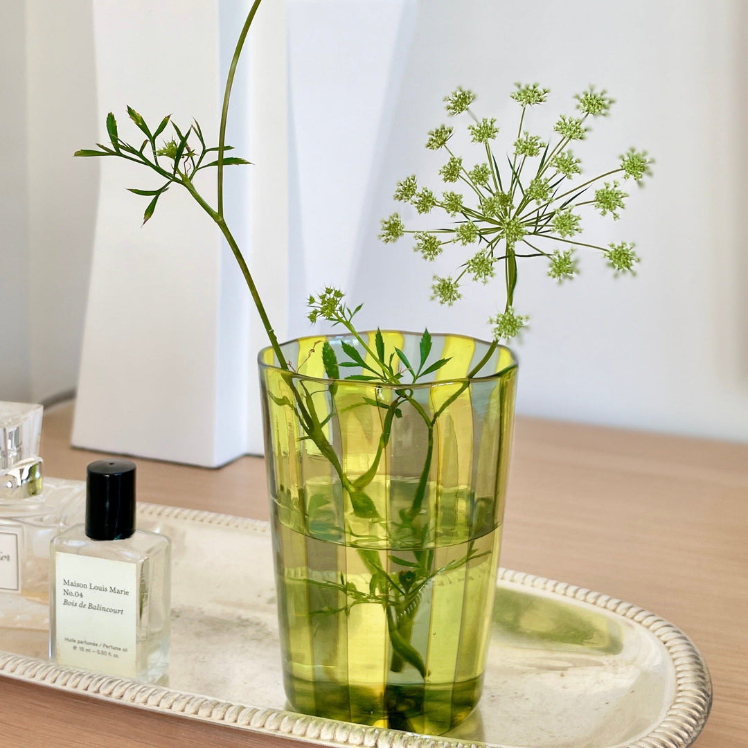 Striped drinking glass from Laguna-B filled with water and decorative green sprigs, displayed on a silver tray.
