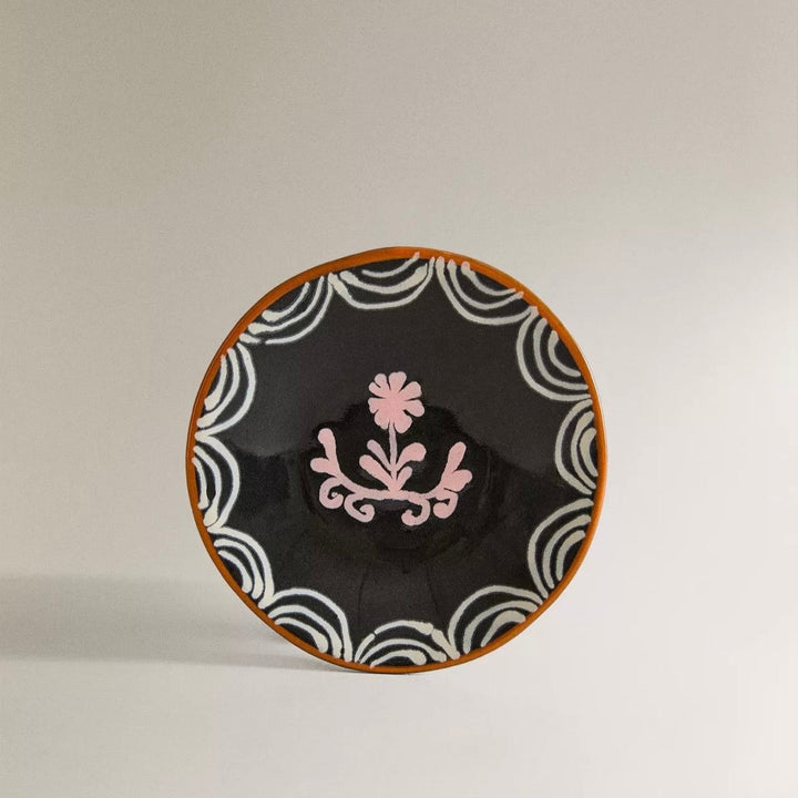 Decorative plate with black background, white wave patterns, and pink floral design on a beige background