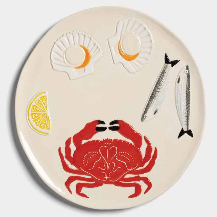 Round cream platter by &Klevering with embossed designs of a crab, seafood, and a lemon wedge.

