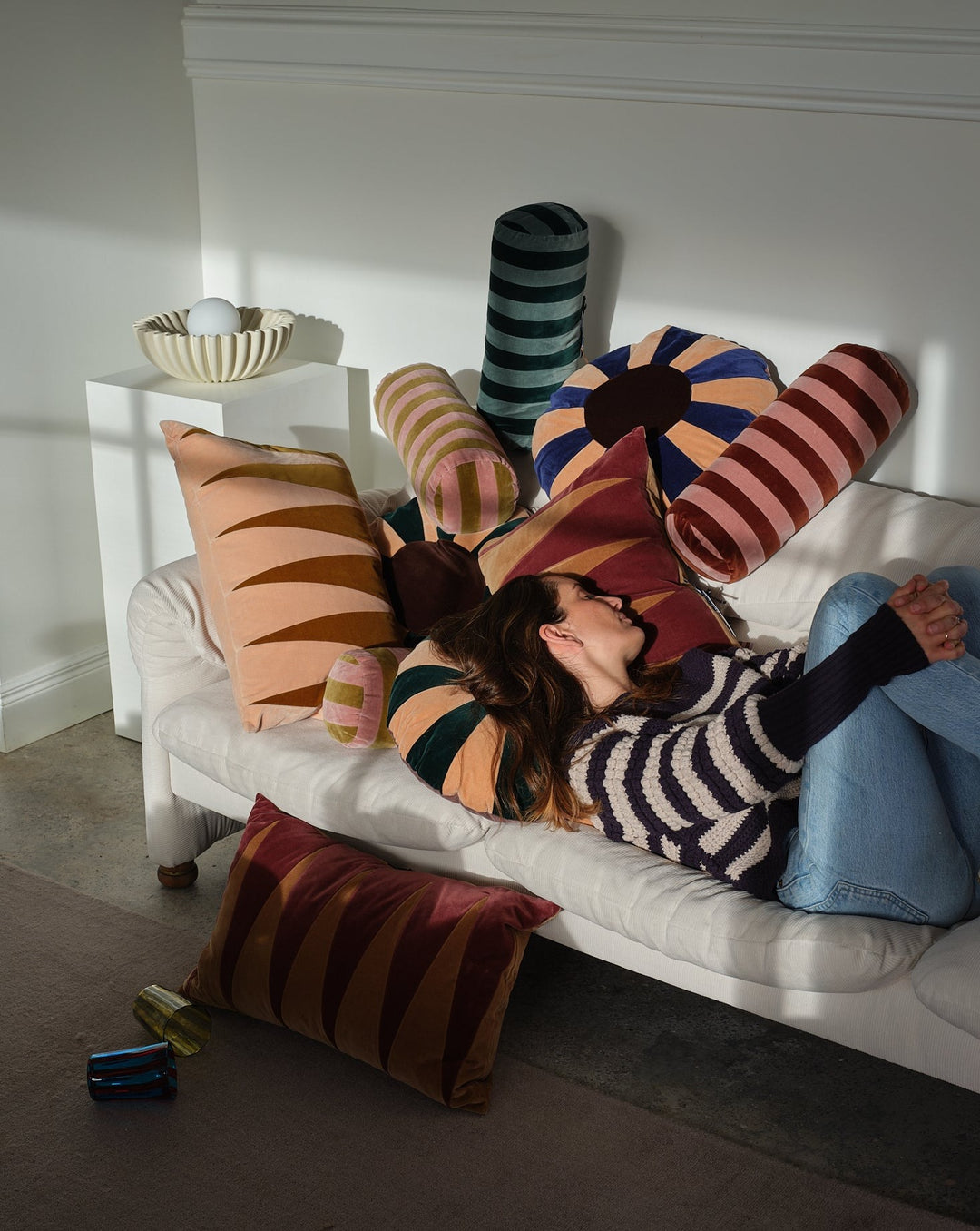 Striped bolster cushion in blue and emerald by Christina Lundsteen, styled with other patterned cushions and a woman lying down.
