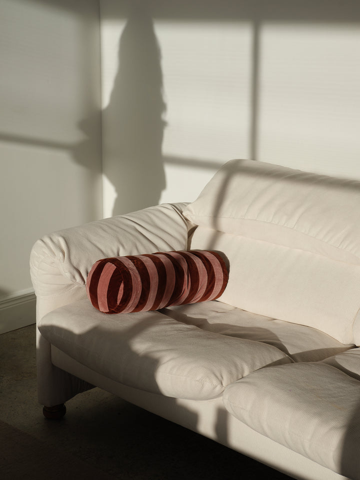 Striped bolster cushion by Christina Lundsteen, featuring blue and emerald stripes, resting on a light-colored corduroy couch.