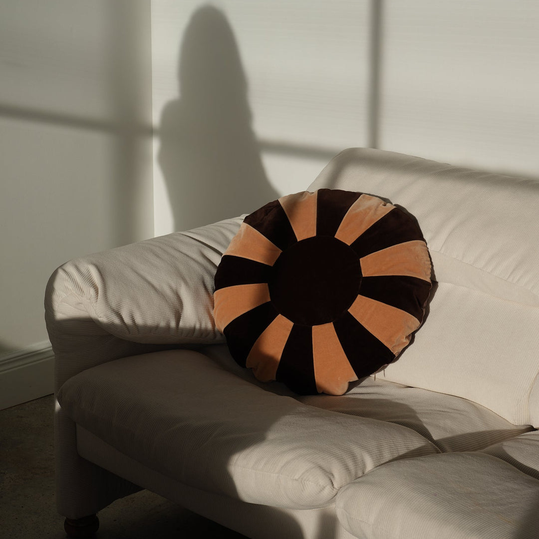 Round chocolate cushion by Christina Lundsteen with a contrasting striped pattern, sitting on an off-white couch.
