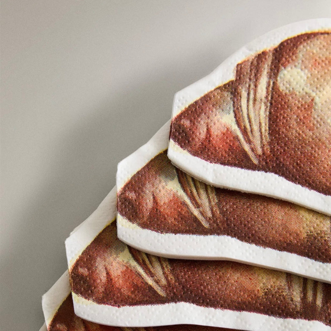 Set of twenty paper napkins with croissant print by Ferm Living, stacked in the corner.