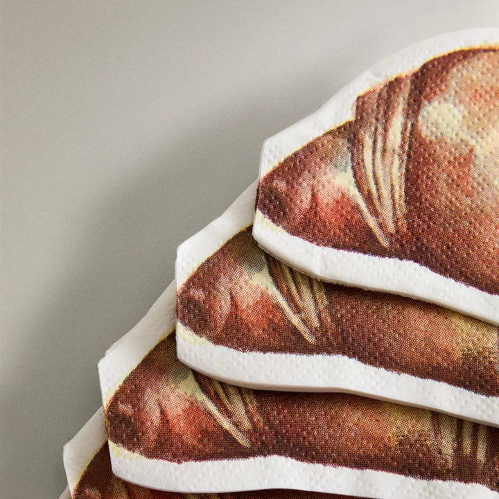 Set of twenty paper napkins with croissant print by Ferm Living, stacked in the corner.