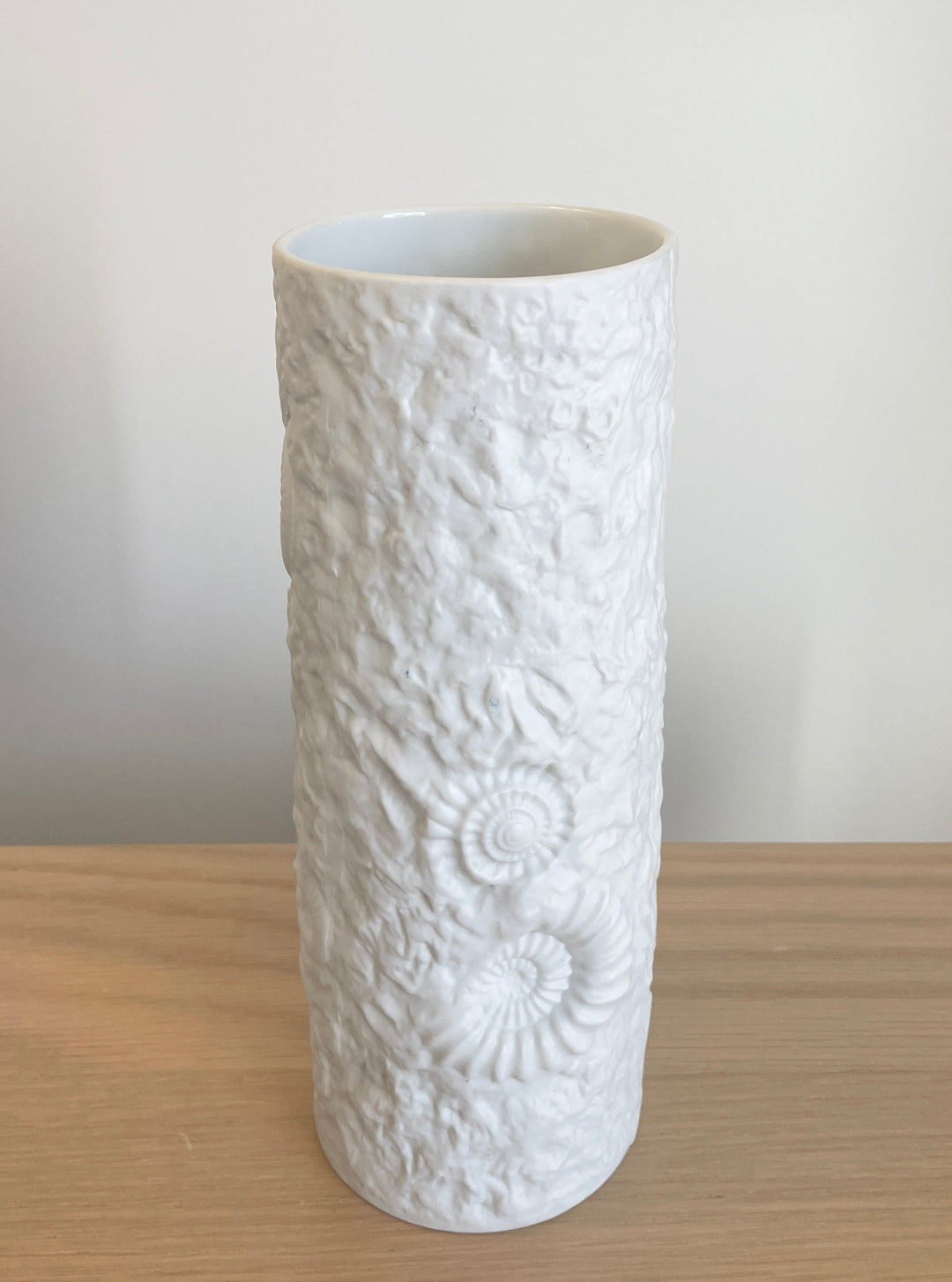 White porcelain vase with fossil pattern by Kaiser, featuring textured, cylindrical form on wooden table.