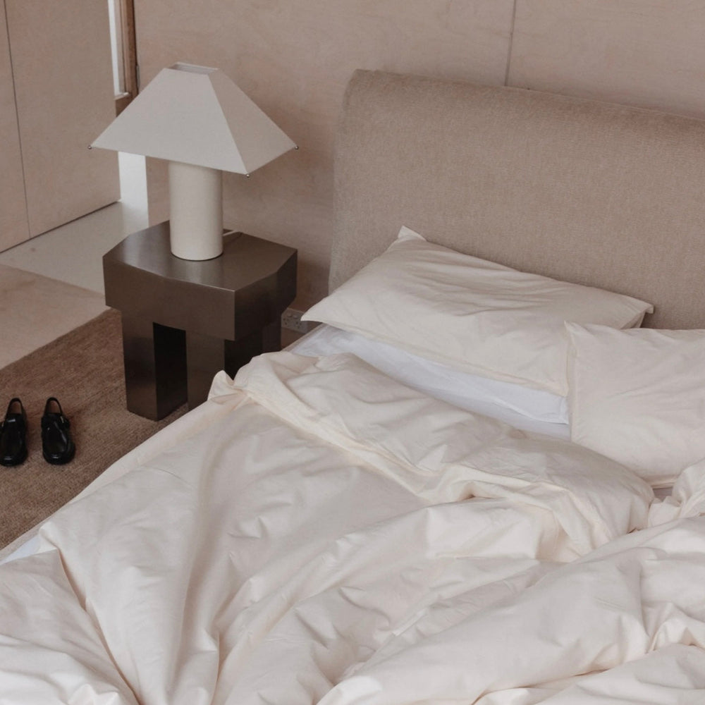 Modern side table by McMullin with a unique geometric design and dark gray finish, next to a made bed.