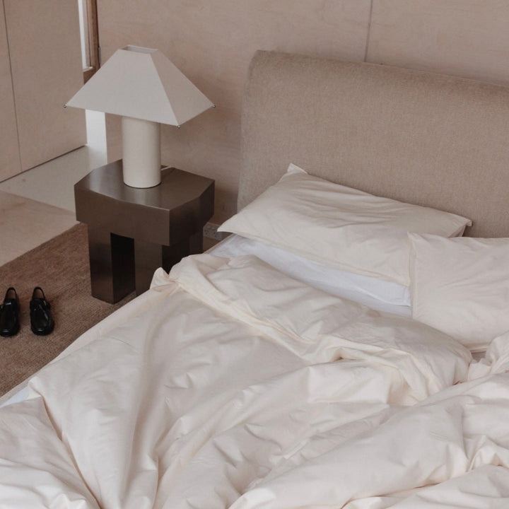 Modern side table by McMullin with a unique geometric design and dark gray finish, next to a made bed.