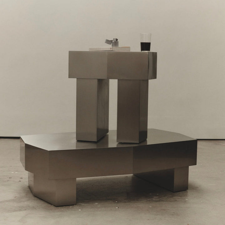 Silver metal side table by McMullin with a lighter and a drink on top.
