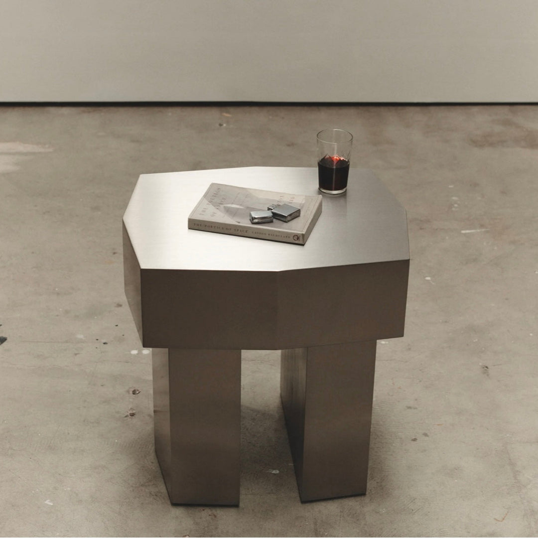 Metal McMullin Rocco Side Table by McMullin with a glass and book on top, sitting on a concrete floor.
