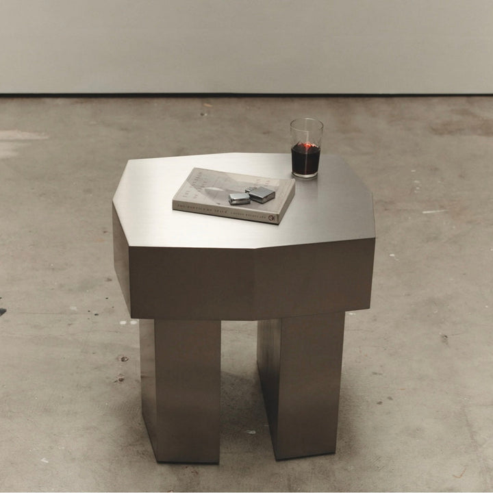 Metal McMullin Rocco Side Table by McMullin with a glass and book on top, sitting on a concrete floor.
