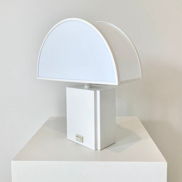 White table lamp by Harvey Guzzini with a semi-circular layered shade, sitting on a matching white square base.