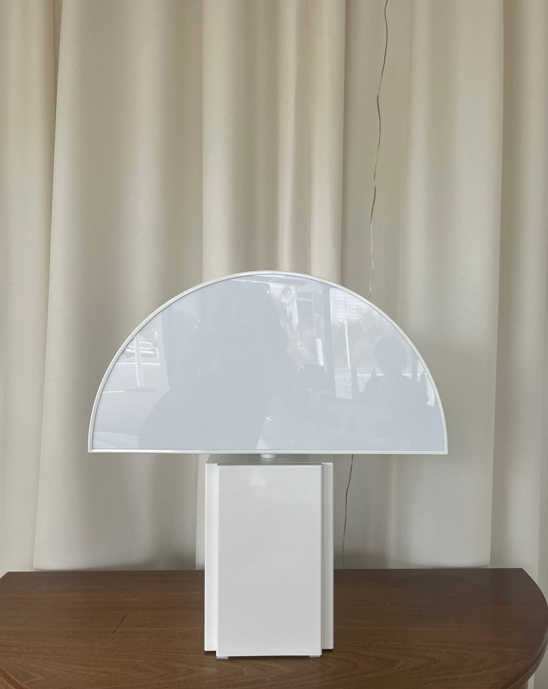White table lamp by Harvey Guzzini from the 1970s, with a semicircle shade and square base on a wooden table.