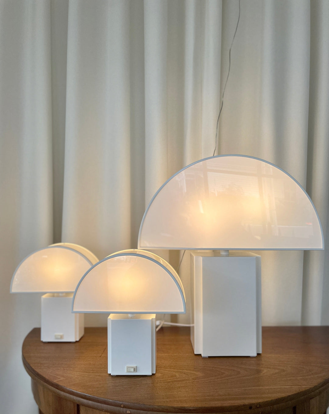 White table lamp by Harvey Guzzini, featuring a semi-circular shade on a rectangular base, sitting on a wooden surface.
