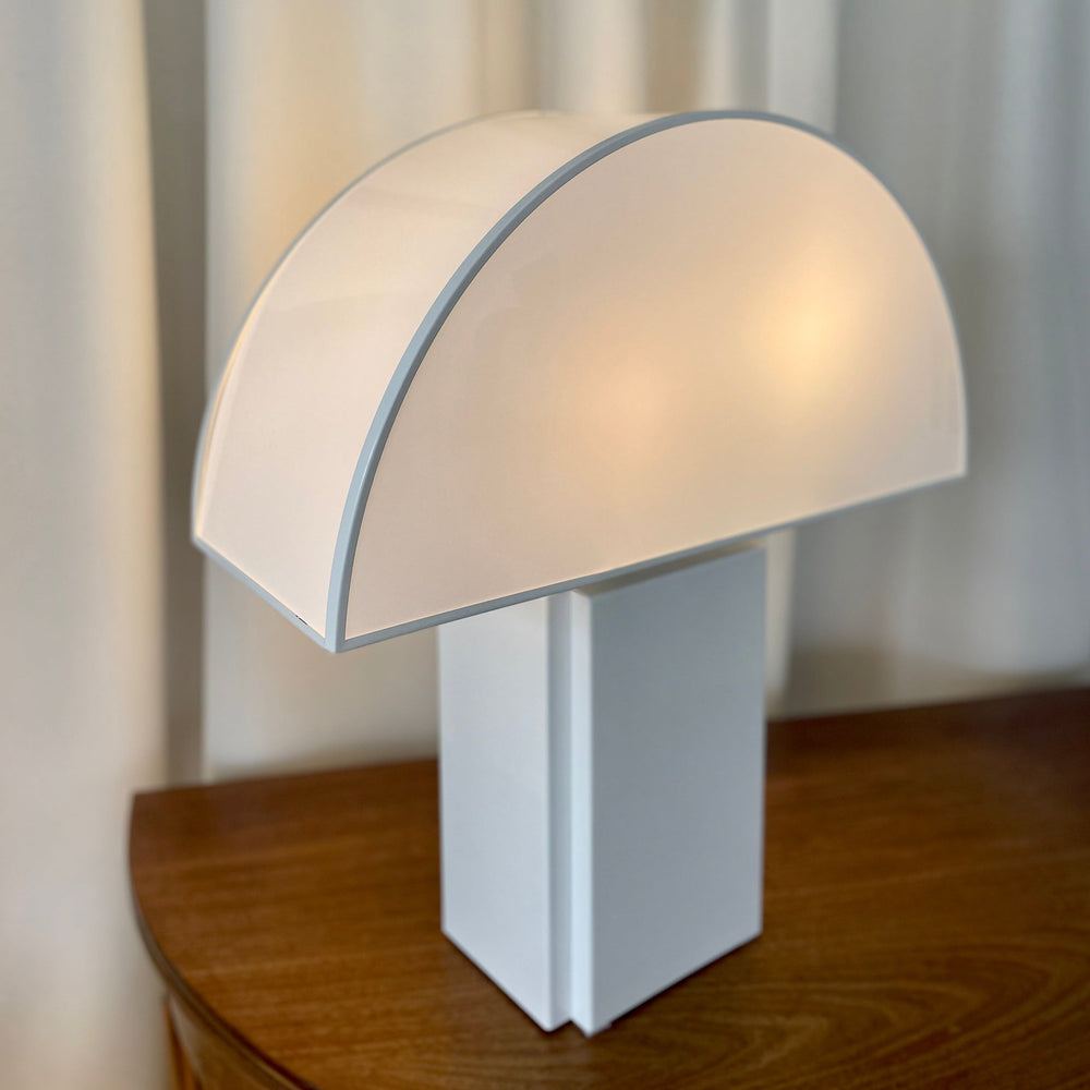 White Olympe table lamp from Harvey Guzzini, featuring a semi-circular shade and a cubic base.