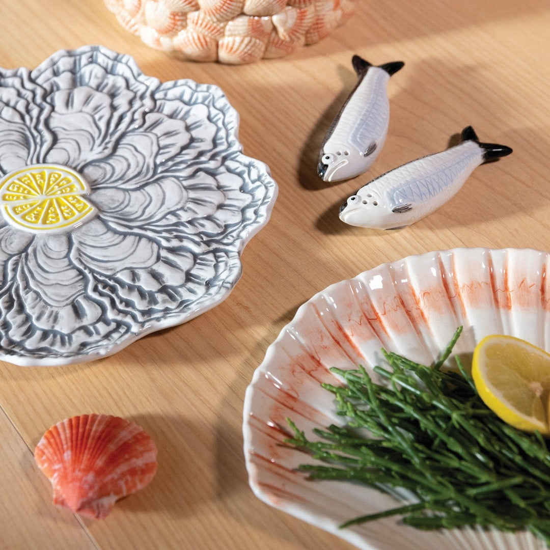 Shell serving plate by &klevering with orange accents, displayed on a wooden surface with green garnish and lemon.