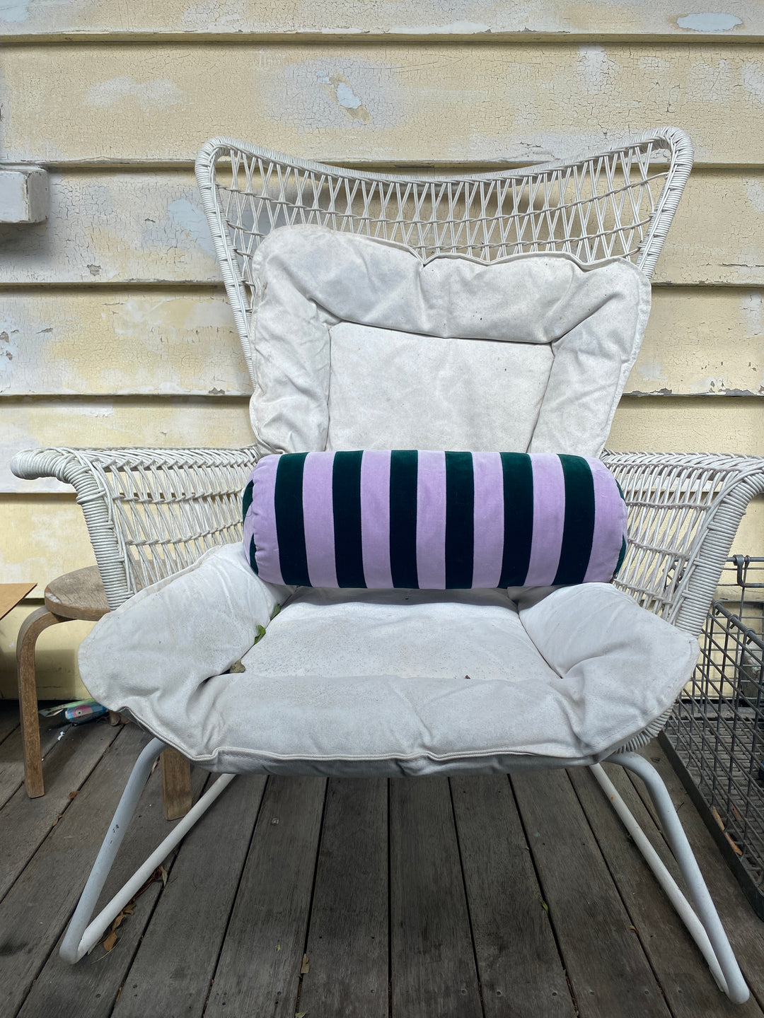 Striped bolster cushion by Christina Lundsteen with emerald and blue stripes resting on a white woven chair.
