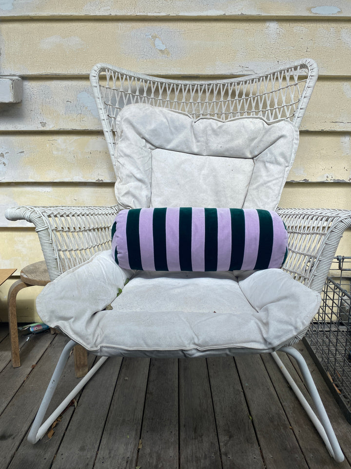 Striped bolster cushion by Christina Lundsteen with emerald and blue stripes resting on a white woven chair.
