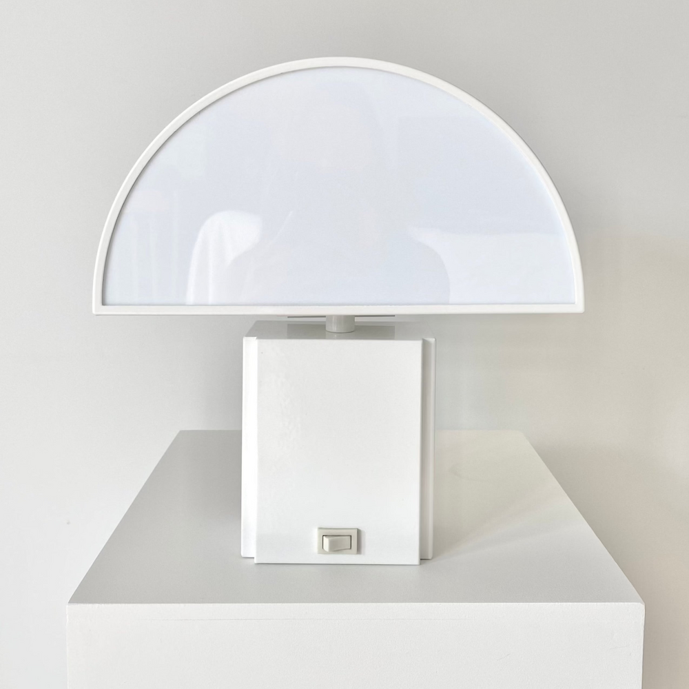 White Olympe table lamp from Harvey Guzzini, with a semi-circular shade, resting on a white surface.