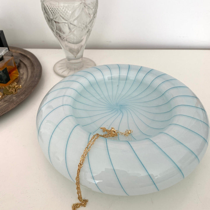White decorative bowl with blue stripes, signed from the 1960s, holding a gold necklace.