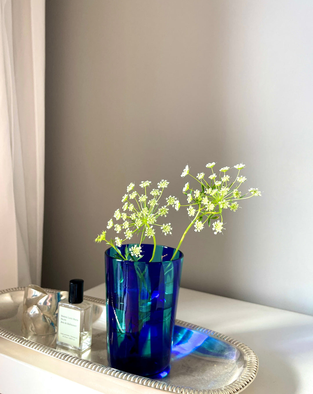 Yellow and steel tumbler by Laguna-B with wildflowers in a blue glass vase on a silver tray.