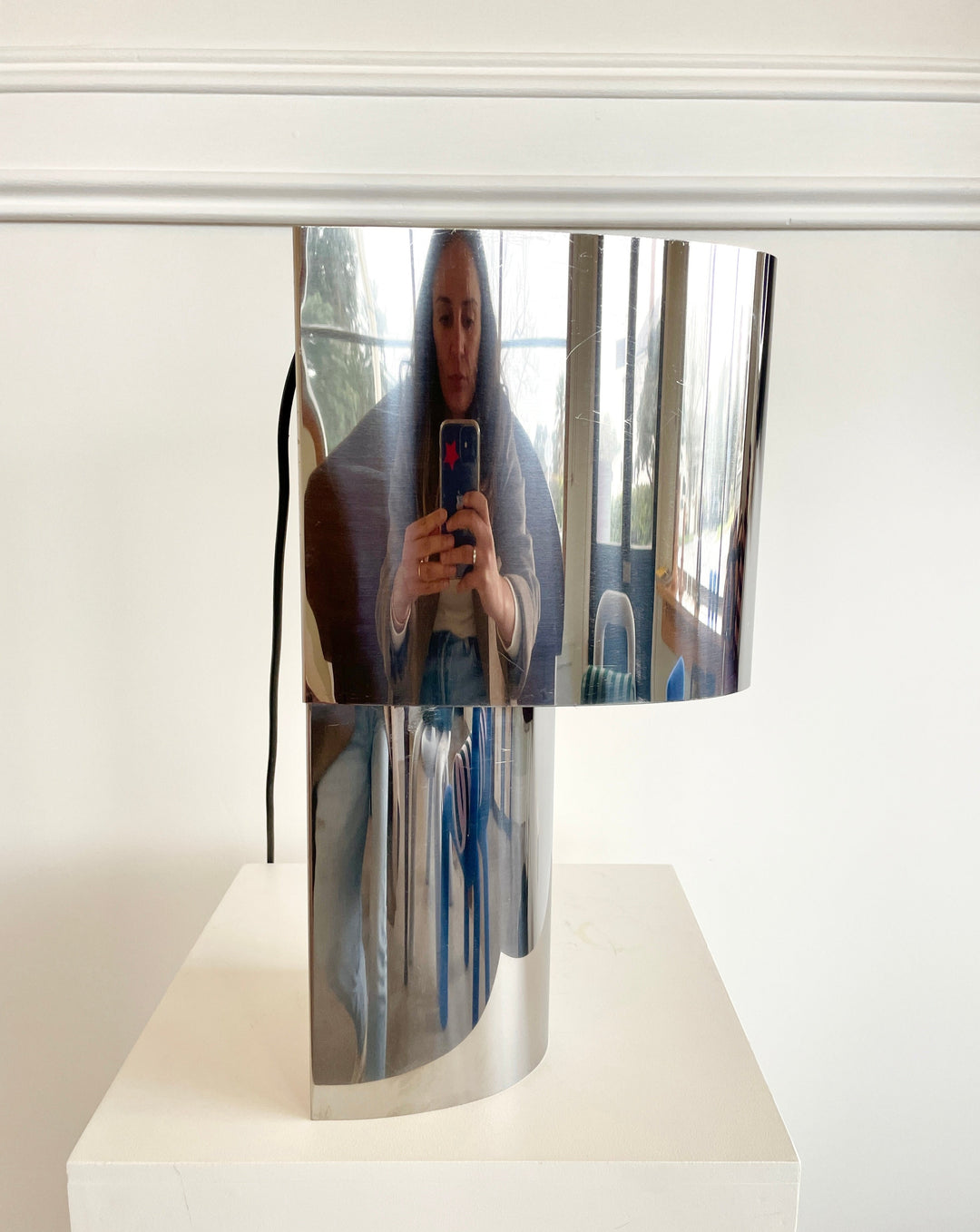 Stainless steel wall and table light from the 1970s, reflected in a mirror on a white pedestal.