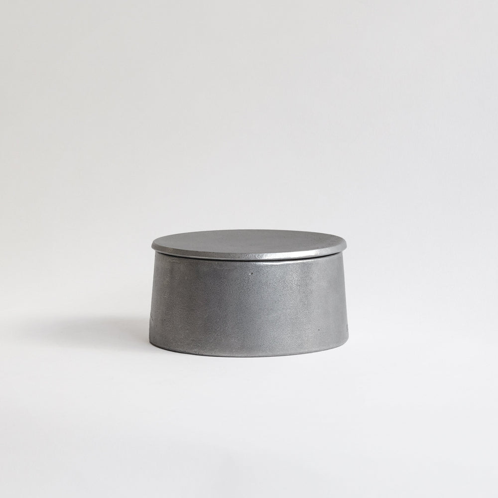 Cylindrical Aluminium candle holder with a lit candle inside on a white background