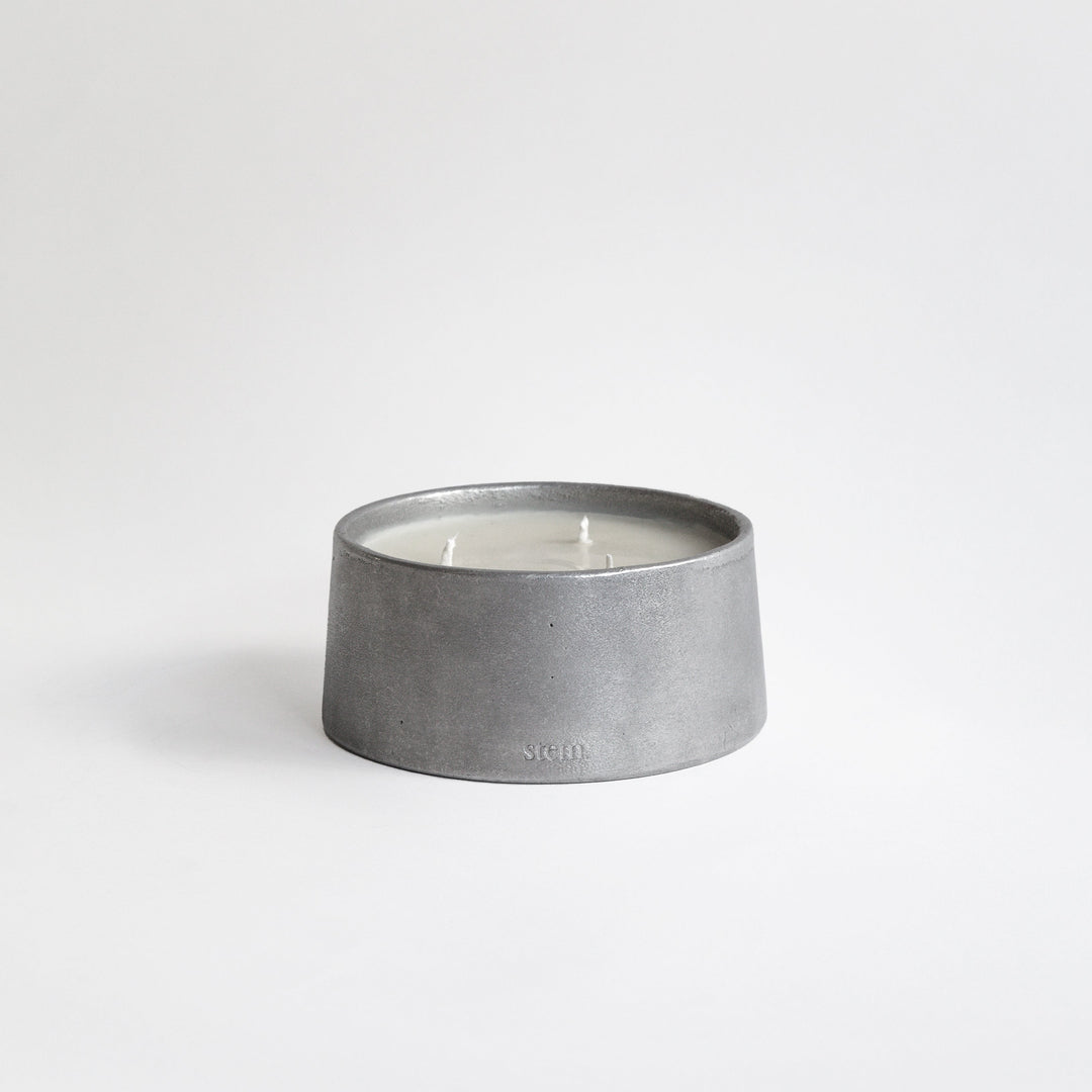 Cylindrical Aluminium candle holder with a lit candle inside on a white background