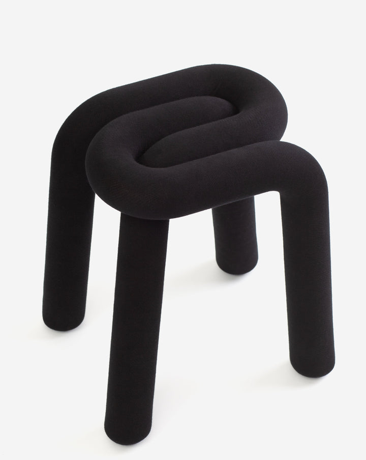 Black upholstered stool by Moustache with a curved top, set on three cylindrical legs.