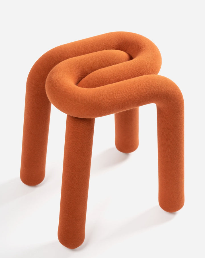 Burnt orange fabric stool by Moustache, featuring a looping design with three legs.