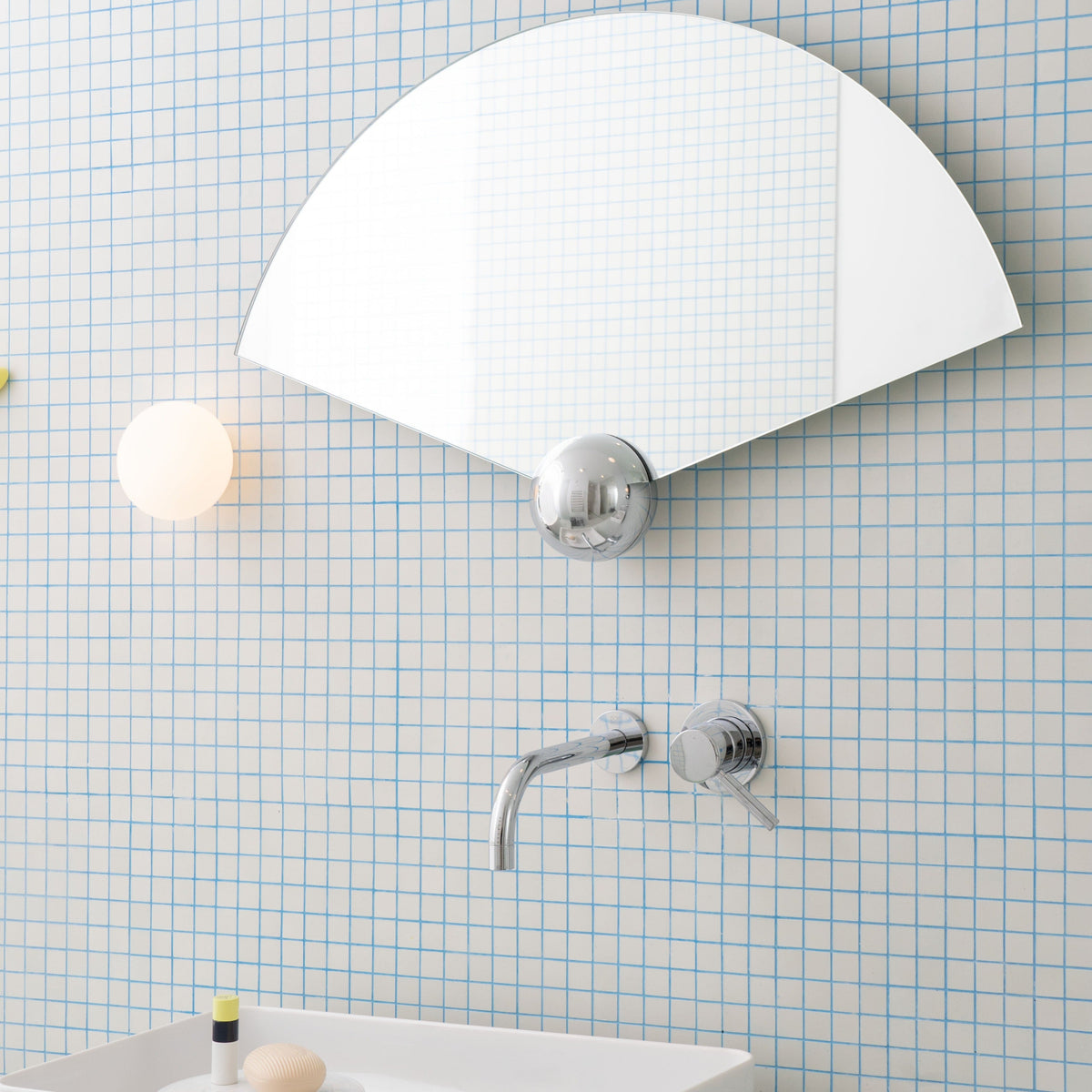 Fan-shaped Sphera wall mirror by Moustache Paris, reflecting a grid-patterned wall in a contemporary bathroom.
