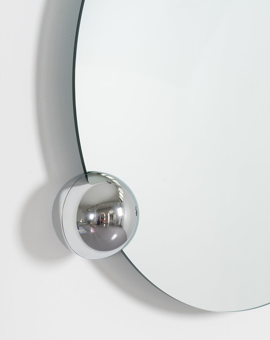 Round wall mirror by Moustache Paris featuring a chrome sphere accent attaching it to the white wall.
