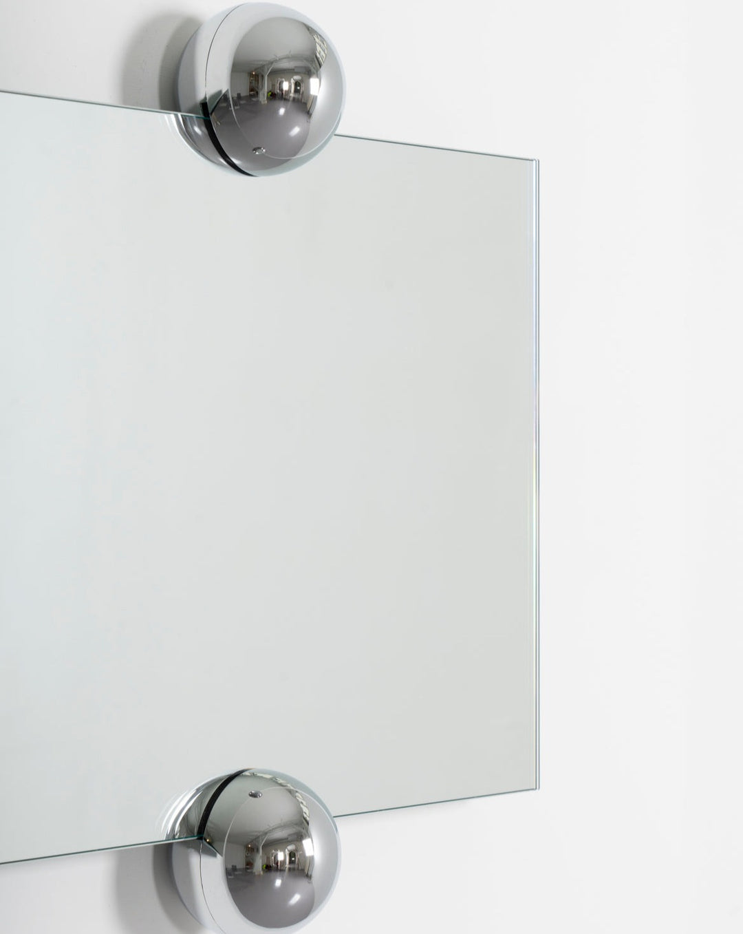 Modern frameless wall mirror by Moustache Paris with rounded chrome spherical supports.