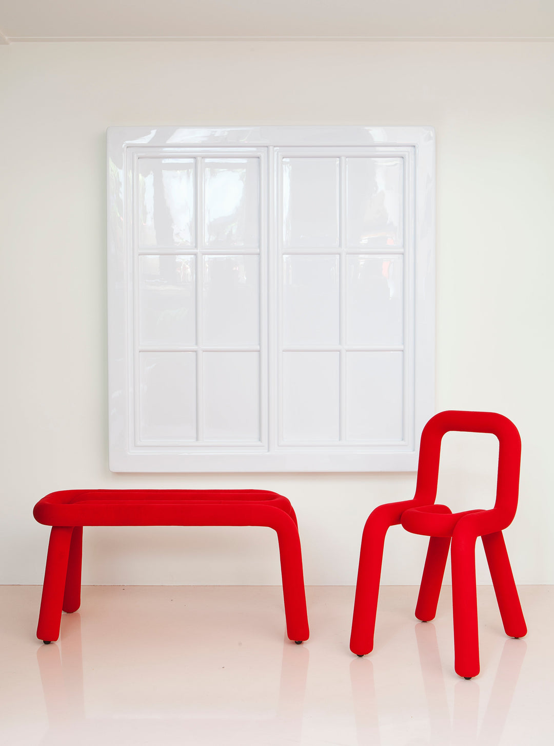 Red tubular chair by Moustache Paris with a matching bench in a minimalist interior.
