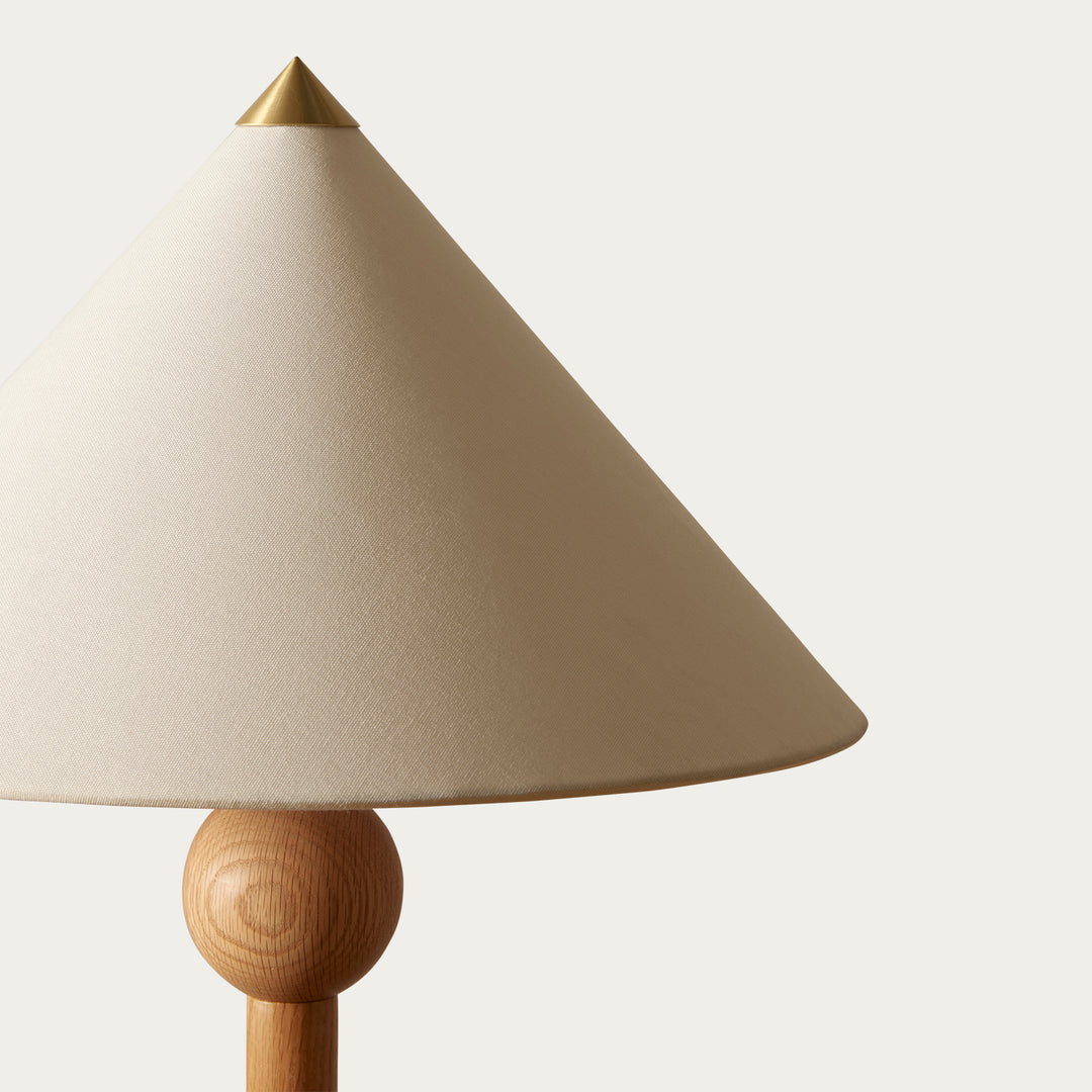 Beige floor lamp by McMullin with a wood base and brass accent on top of the lampshade.