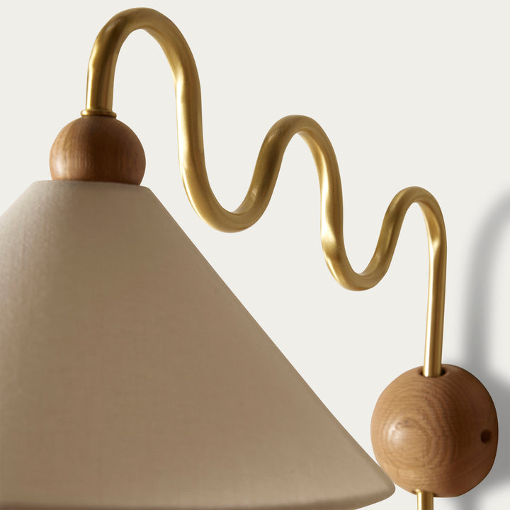 Wall sconce by McMullin with a wavy gold metal arm and a beige fabric shade.
