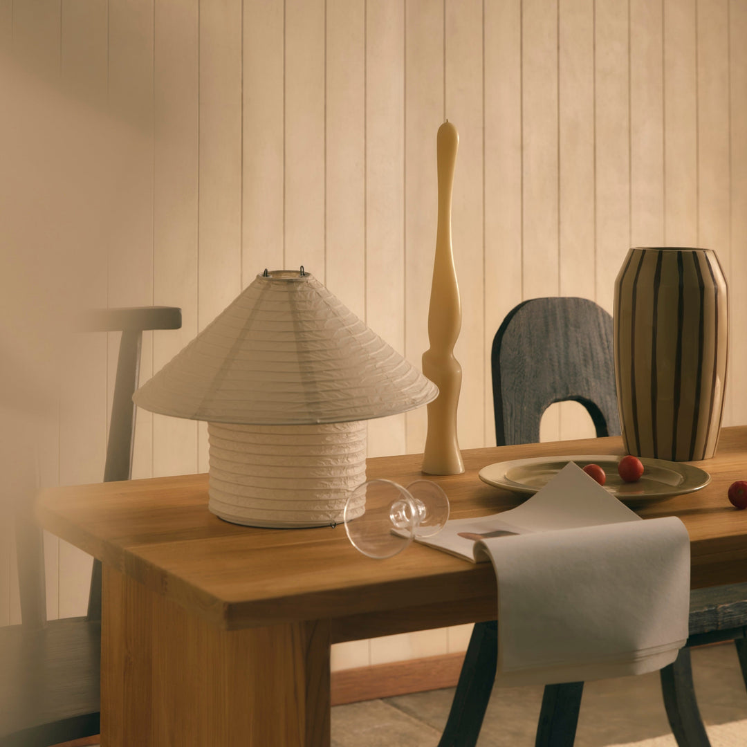 Rice paper table lamp by McMullin with a pleated shade, on a wooden table with decorative items.