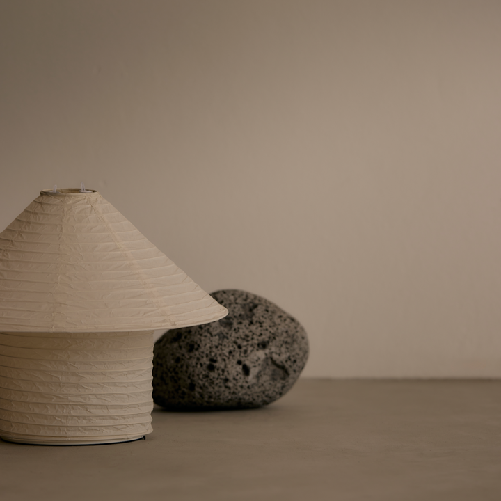 Rice paper table lamp by McMullin, next to a grey porous rock on a neutral surface.